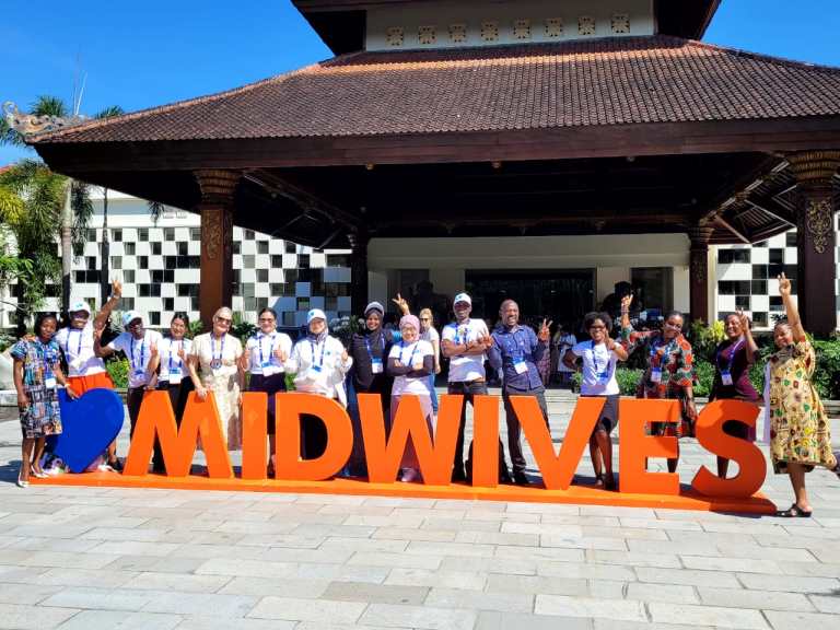 Group photo of midwives from around the world infront of a big sign with the word MIDWIVES outside the ICM Congress in Bali.