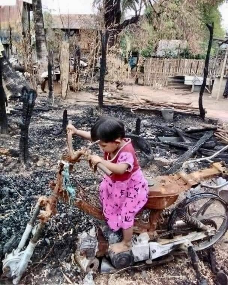 A picture of a small girl riding on a burned skeleton of a motorcycle in Myanmar.
