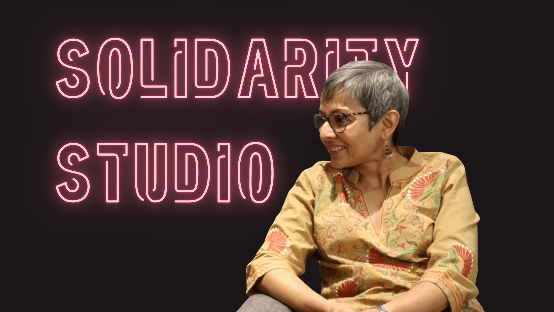 Pink neon text on Black background with the words SOLIDARITY STUDIO and the profile of Lopa Banerjee in a yellow tunic.