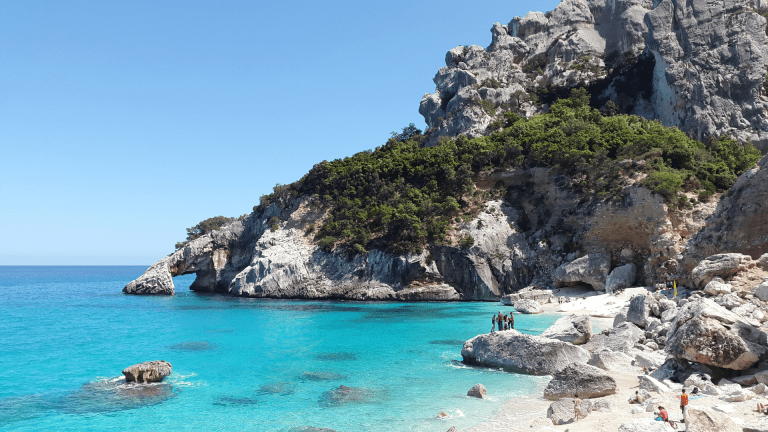 A photo of a coastline of the Mediterranean sea, with beautiful waters and people enjoying nature.