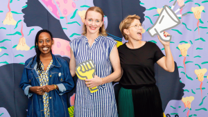 Amina Umuhoza, Margaret Butler and Julia Wiklander outside of the Solidarity Studio. They are standing in front of a large illustration of the portraits of women.